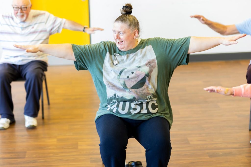elderly-people-exercising-11674390 Seniors participating in a seated exercise class, promoting community health and active aging.