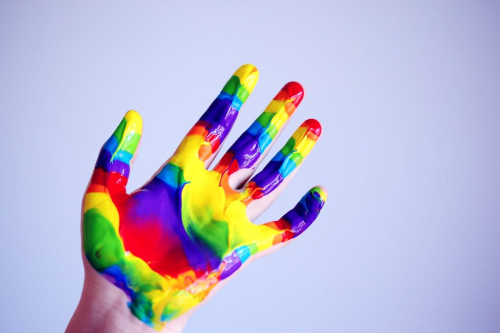 person-s-hand-with-paints-1174932 A vibrant hand covered in rainbow paint against a plain background, symbolizing creativity.