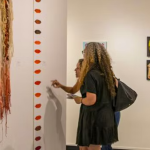 Two women are appreciating an art piece that represents different colored lips. Arts Fort Worth offers resources for selling art.