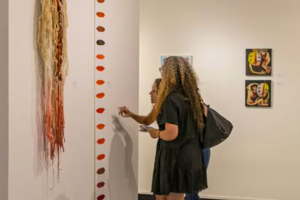 Two women are appreciating an art piece that represents different colored lips. Arts Fort Worth offers resources for selling art.